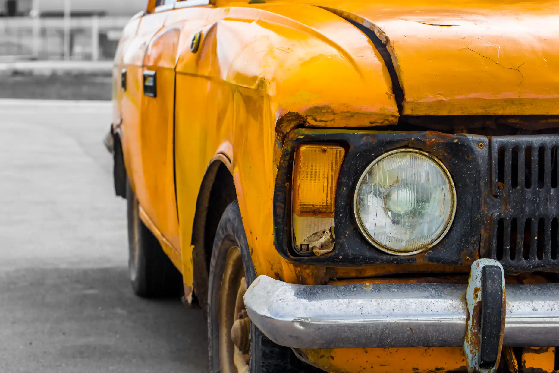 Damaged old yellow car front end Close-up of a damaged old yellow car with a dented front guard, rusty grille and cracked indicator lens